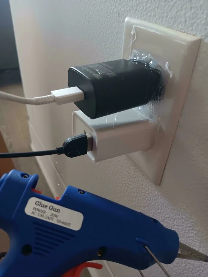 Black and white chargers attached to an electrical outlet with glue gun adhesive showing incorrect electronics handling.