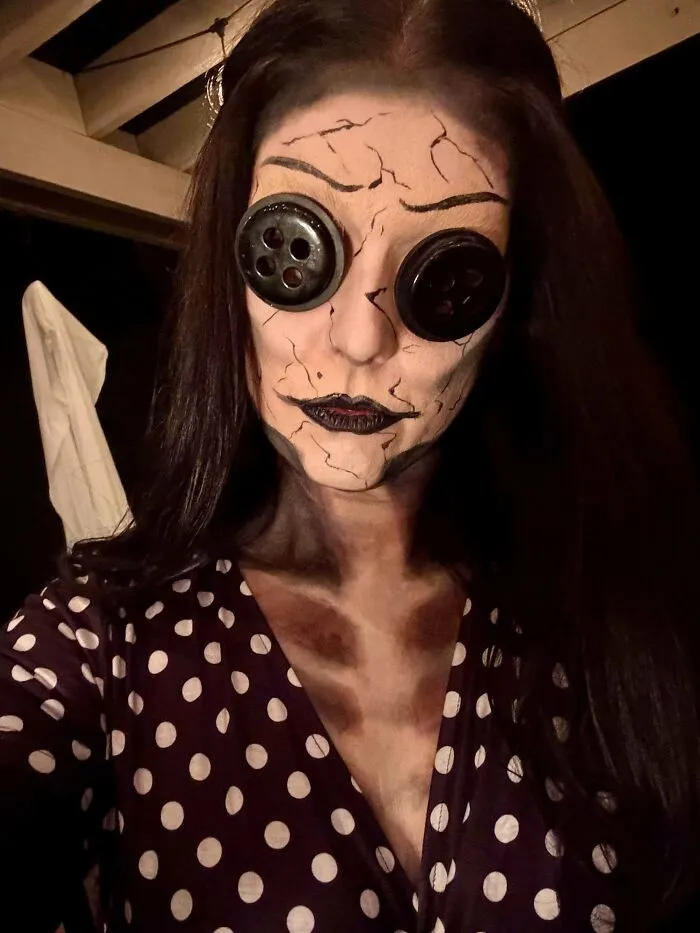 Woman in a genius Halloween costume with cracked makeup and large button eyes, perfect for making the party talk.