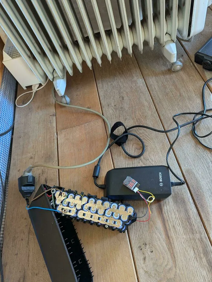 Exposed electronics battery pack and charger on wooden floor with tangled wires showing improper handling.