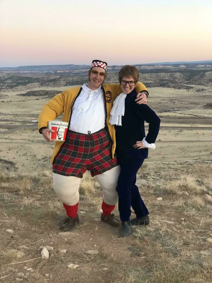 Two people outdoors wearing genius Halloween costumes, one holding a Kentucky Fried Chicken bucket, posing and smiling.