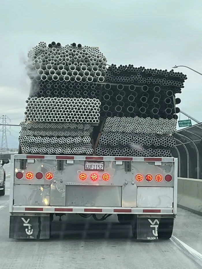 Truck carrying large stacks of hollow pipes with repetitive holes creating a trypophobia nightmare fuel pattern.