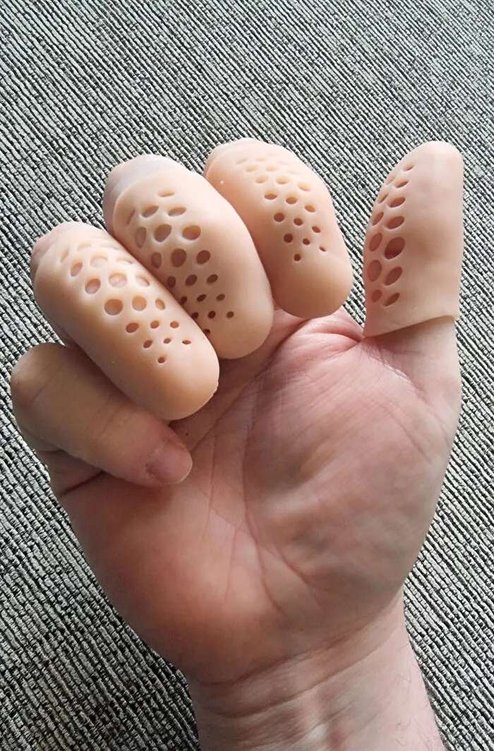 Hand wearing silicone finger covers with multiple holes, creating trypophobia nightmare fuel effect on skin.
