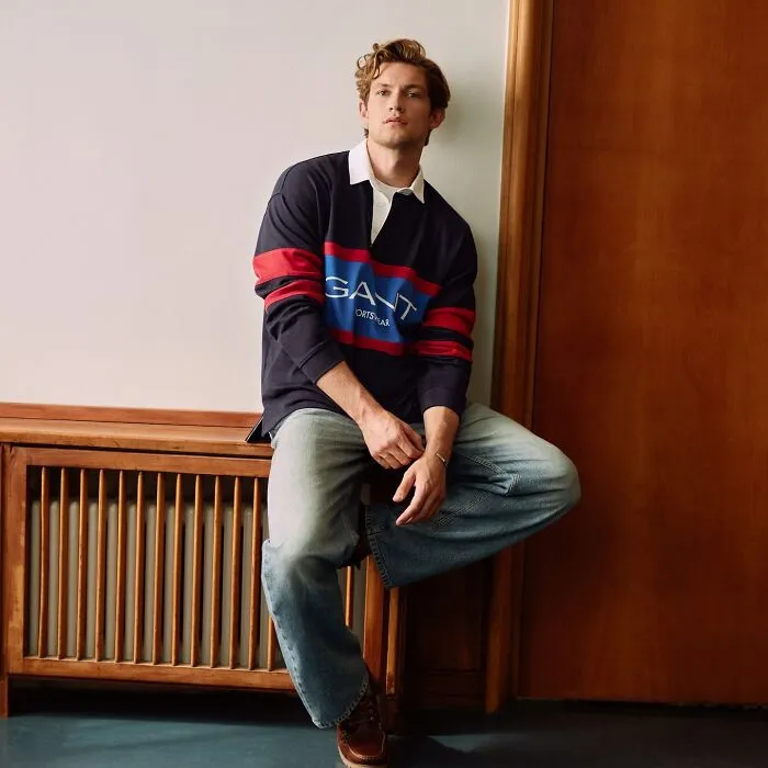 Young Damian Hardung posing casually indoors wearing a navy and red shirt and jeans, representing most handsome man in the world 2025.