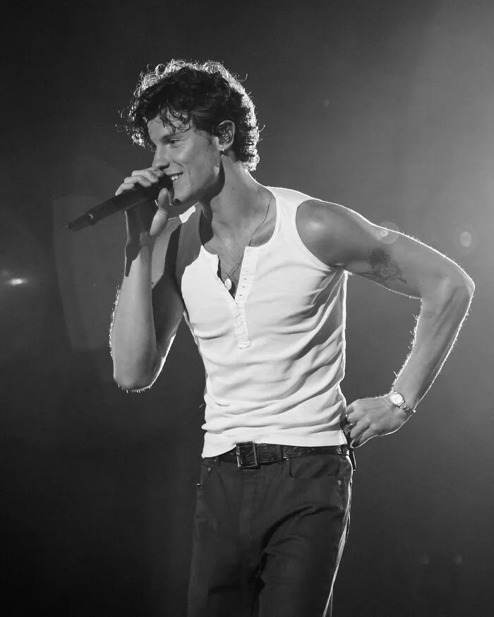 Shawn Mendes performing on stage wearing a white sleeveless shirt and black pants in the contest for most handsome man in the world.