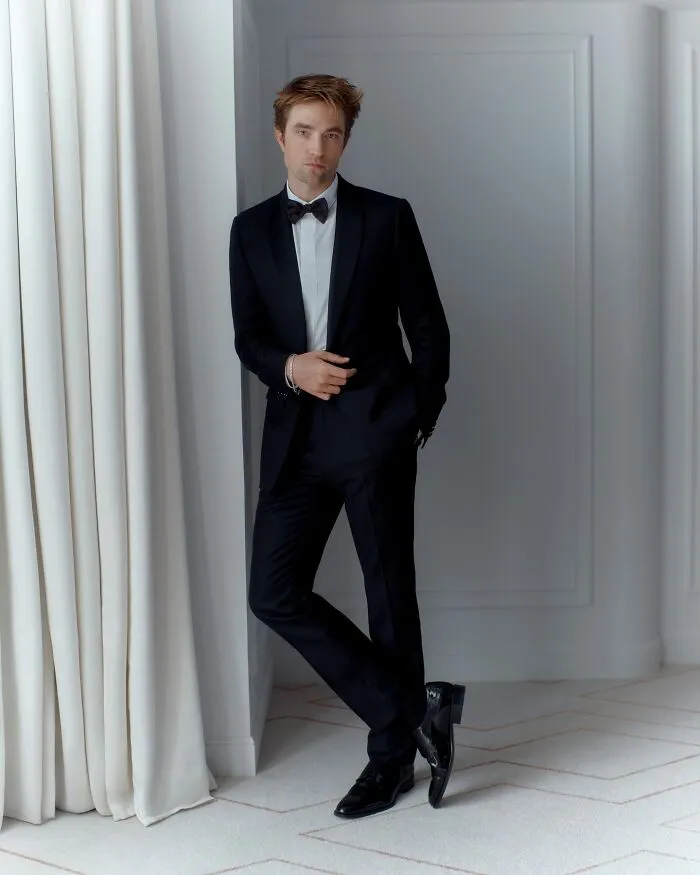 Robert Pattinson dressed in a black tuxedo posing indoors near white curtains for most handsome man in the world 2025.