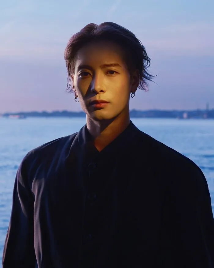 Jackson Wang posing by the water at sunset, showcasing features for the most handsome man in the world 2025.