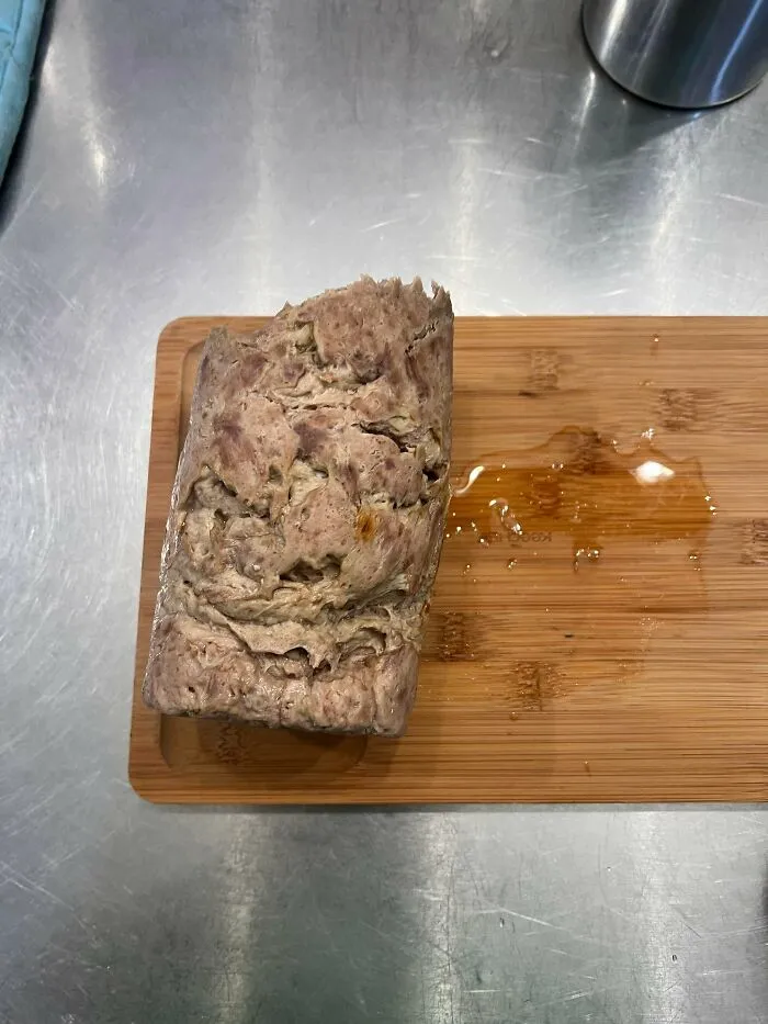 Unholy food pic of an irregular loaf with an unappetizing texture on a wooden cutting board.