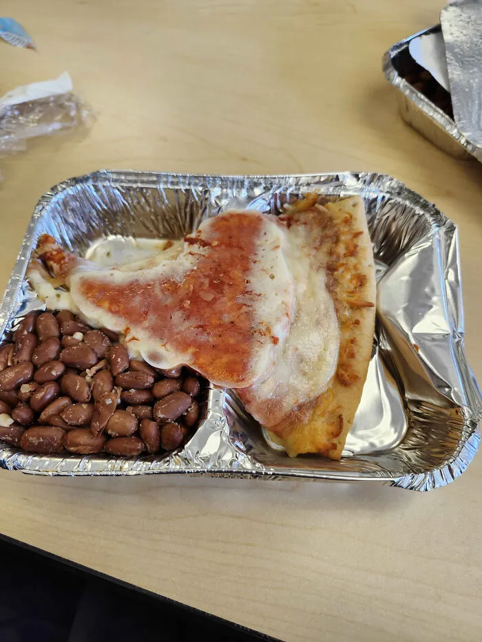 Unholy food pic of two unappetizing pizza slices with beans in a foil tray on a wooden table.