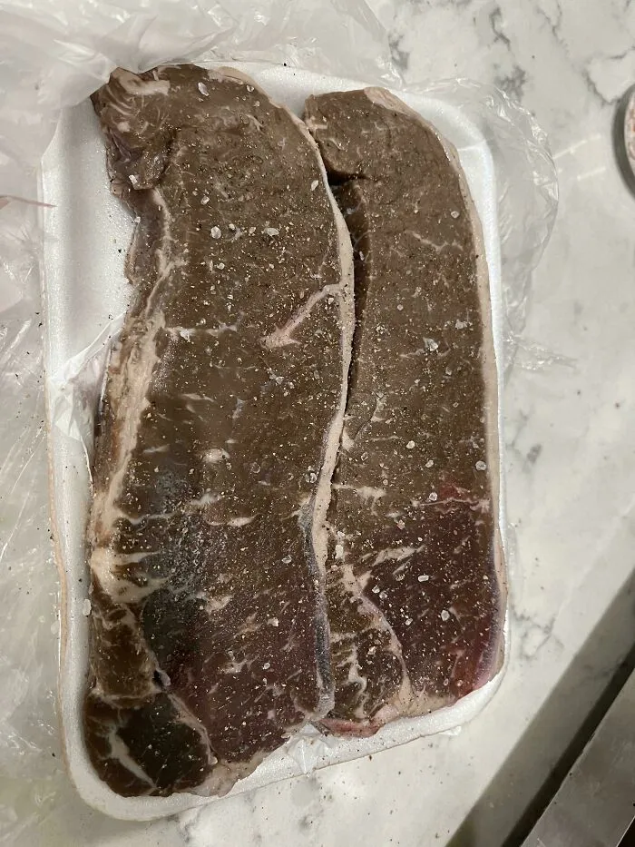 Two frozen, salt-covered raw steaks on a white foam tray, illustrating unholy food pics that look unappetizing.