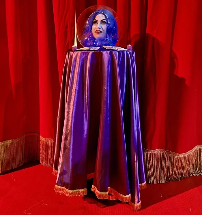 Creative Halloween costume featuring a floating head illusion with purple cape and mystical tarot cards on red curtain backdrop.