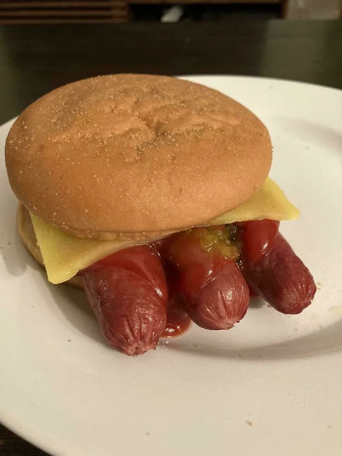 Unholy food pic showing a bizarre sandwich with three hot dogs, cheese, and ketchup on a plain bun on a white plate.