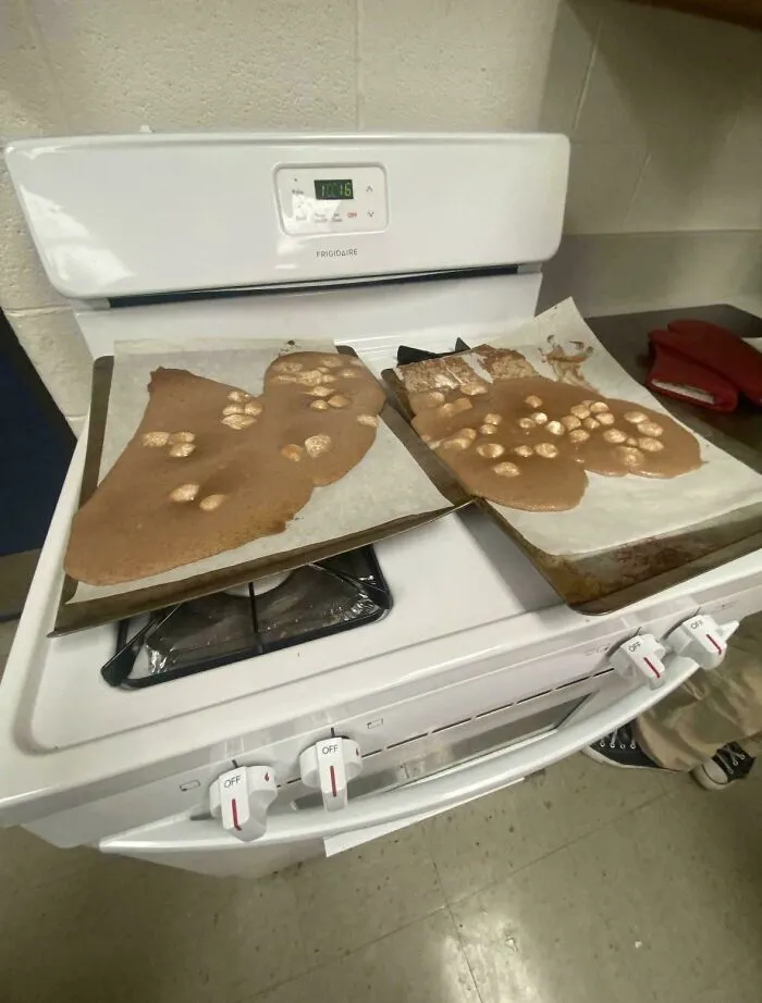 Unholy food pics showing melted, spilled chocolate dessert with marshmallows on baking sheets over a stove.