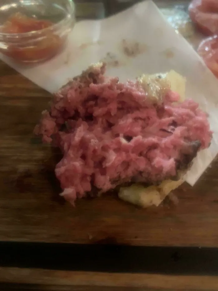 Close-up of unholy food with raw, pink meat on a wooden surface, highlighting unappetizing food pics.