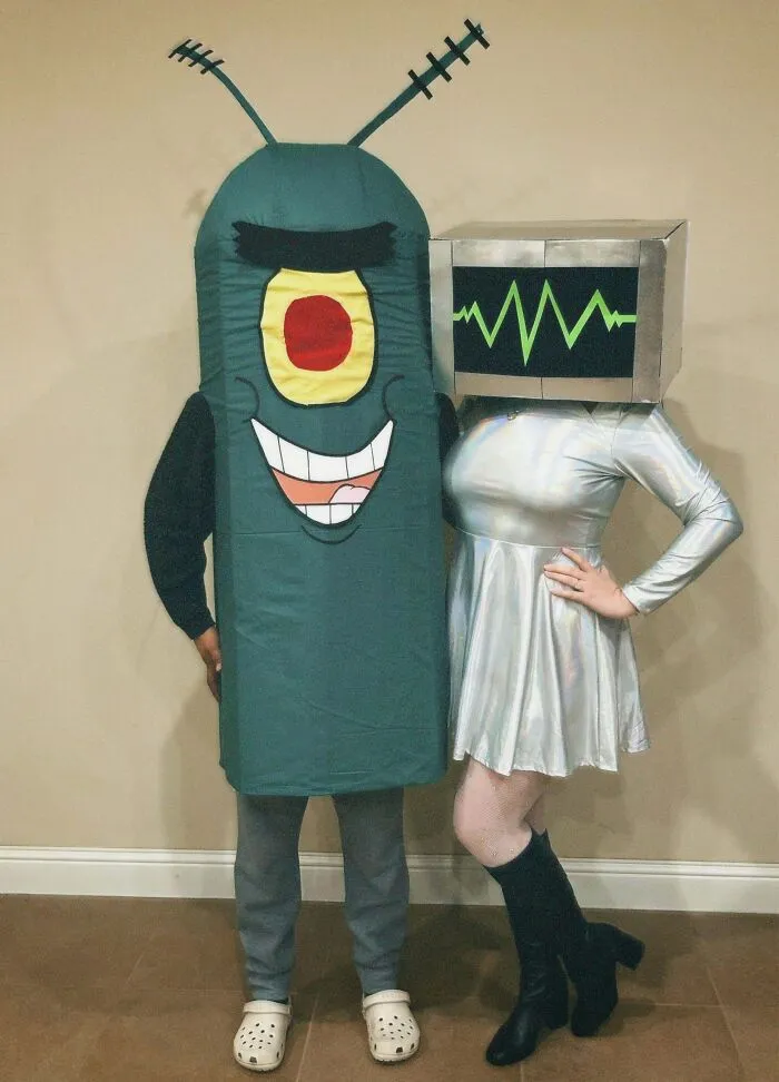 Two people in genius Halloween costumes, one as a green cartoon character and the other with a TV screen head with green waveform.