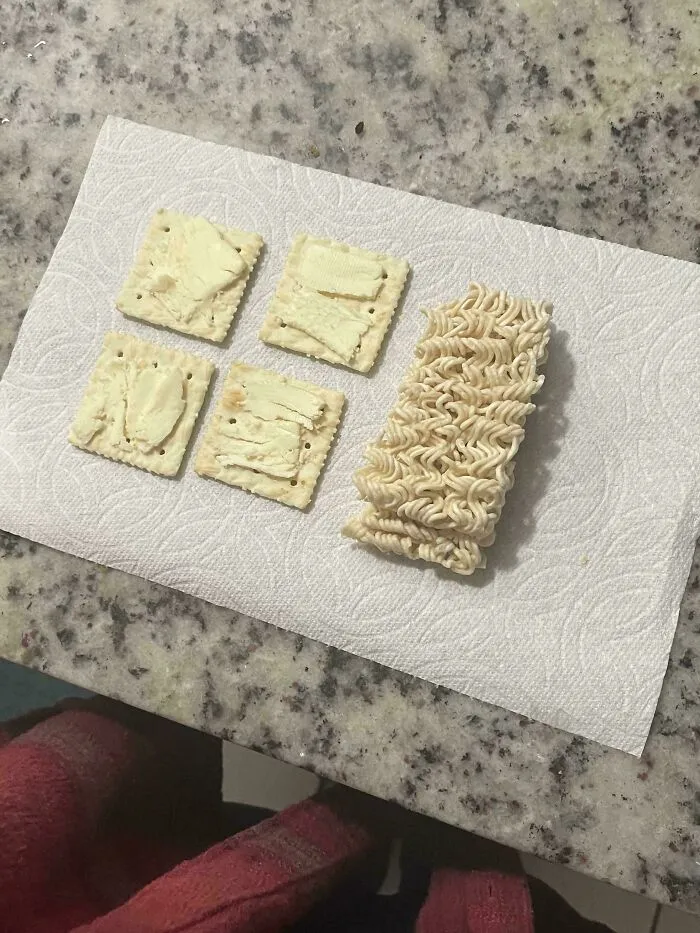 Unholy food pic of crackers smeared with butter next to a block of uncooked instant ramen on a paper towel.