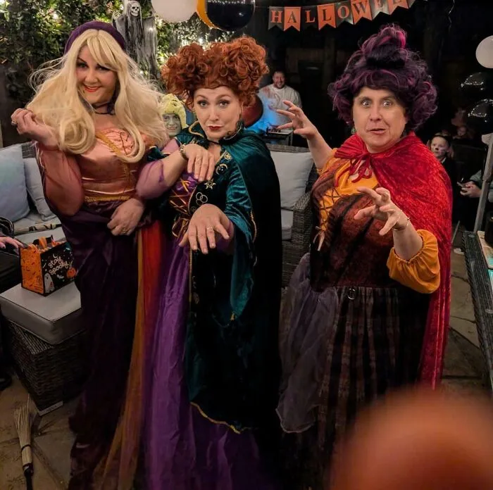 Three women in genius Halloween costumes dressed as witches posing and making spooky gestures at a Halloween party.