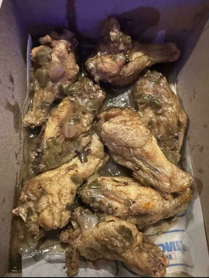 Unappetizing chicken wings covered in an unappealing sauce in a takeout box, an unholy food pic example.