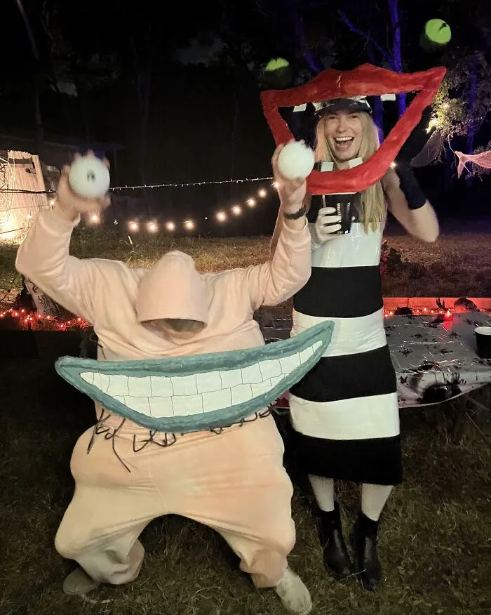 Two people in genius Halloween costumes posing outdoors at night, with creative oversized mouth and eyeball props.