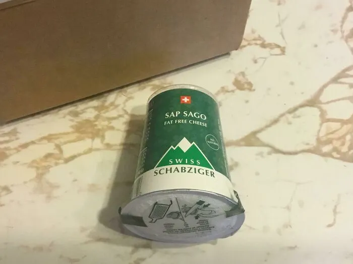 Green Swiss Schabziger fat-free cheese container on a marble surface, an example of unpopular local foods.