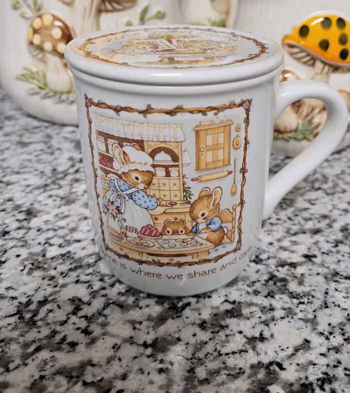 Ceramic mug with whimsical cottage core aesthetics featuring rabbits baking in a rustic kitchen scene on granite countertop.