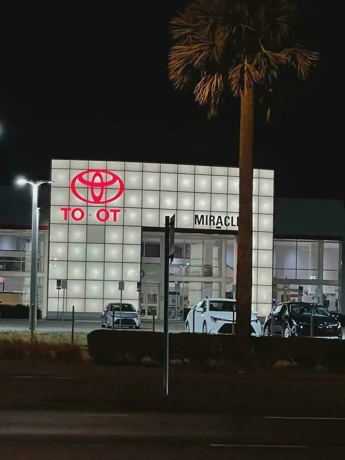 LED sign at a car dealership with illuminated panels and a partially lit brand logo visible at night.
