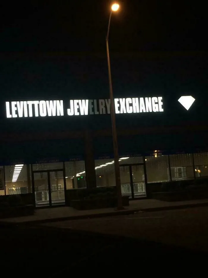 LED sign for Levittown jewelry exchange with a bright diamond icon, partially obscured by a street lamp at night.