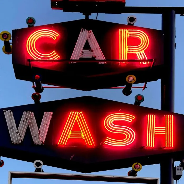 Neon LED signs displaying car wash in bright red and yellow lights against a clear evening sky.