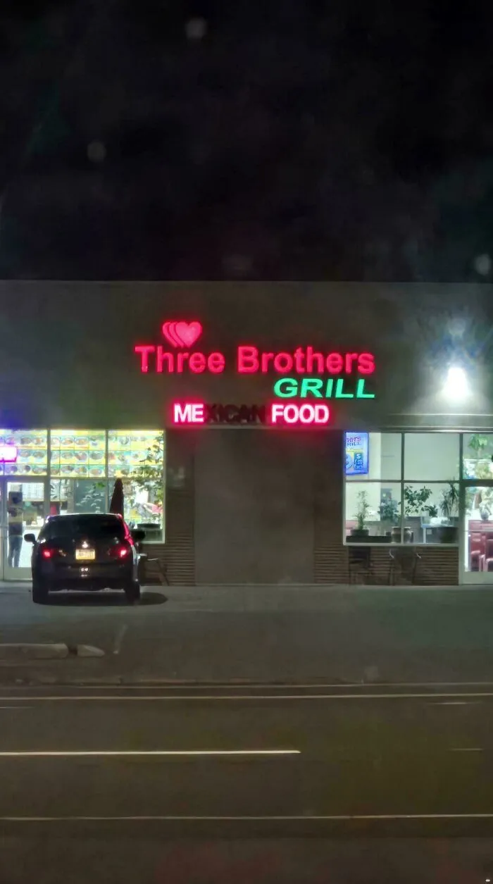 Three Brothers Grill LED sign glowing red and green above the restaurant entrance at night.