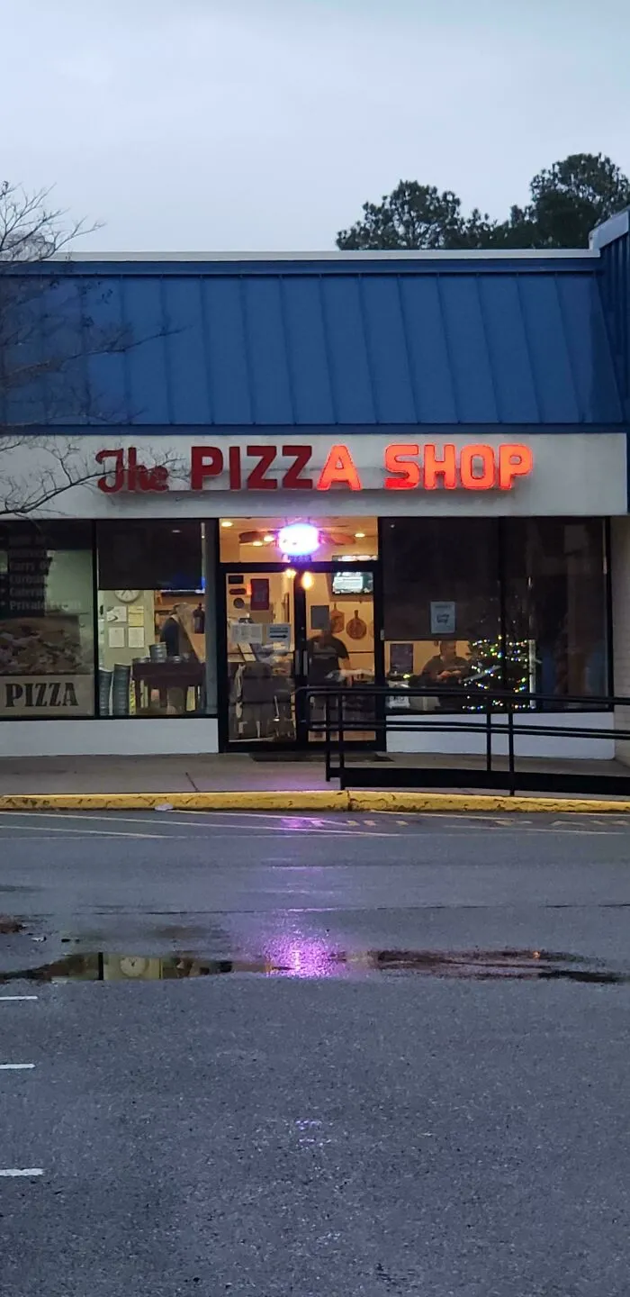 LED pizza shop sign glowing red above entrance of a small local restaurant during early evening hours.