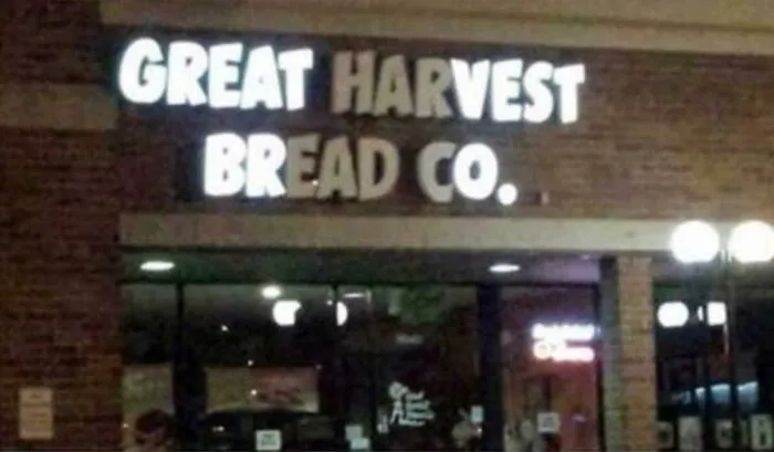 LED sign displaying Great Harvest Bread Co with uneven and partially lit letters on a brick building facade at night.