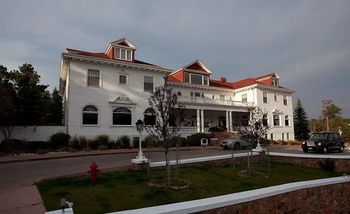 Large white historic house surrounded by trees under cloudy sky, a spooky destination perfect for Halloween visits.