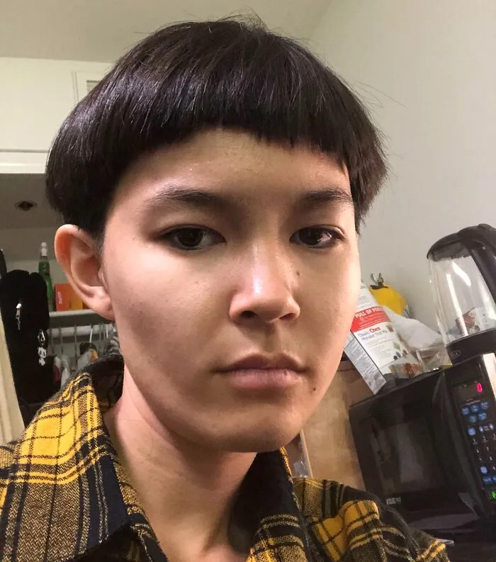 Joven con accidente de cabello hilarantemente trágico, corte de cabello irregular y expresión seria en interior.