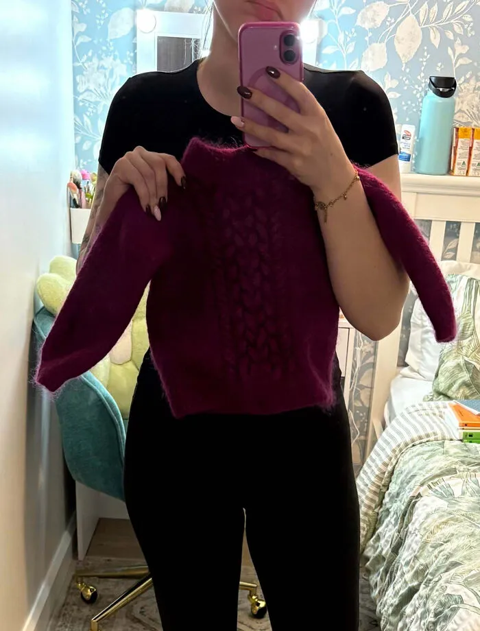 Persona sosteniendo un suéter pequeño color púrpura frente a un espejo en un dormitorio, mostrando que siempre puede empeorar.