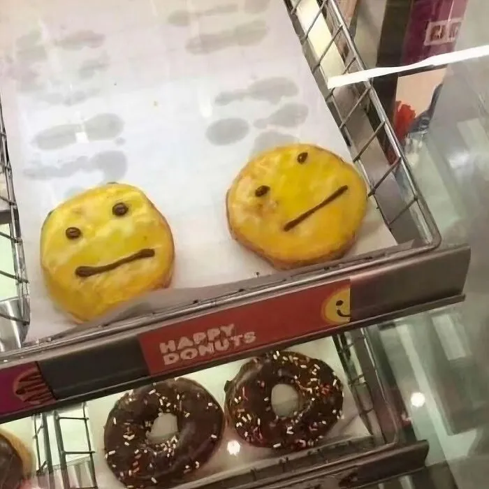 Donas bizarras con cara extraña y expresión inexpresiva en vitrina de exhibición de tienda de donas.