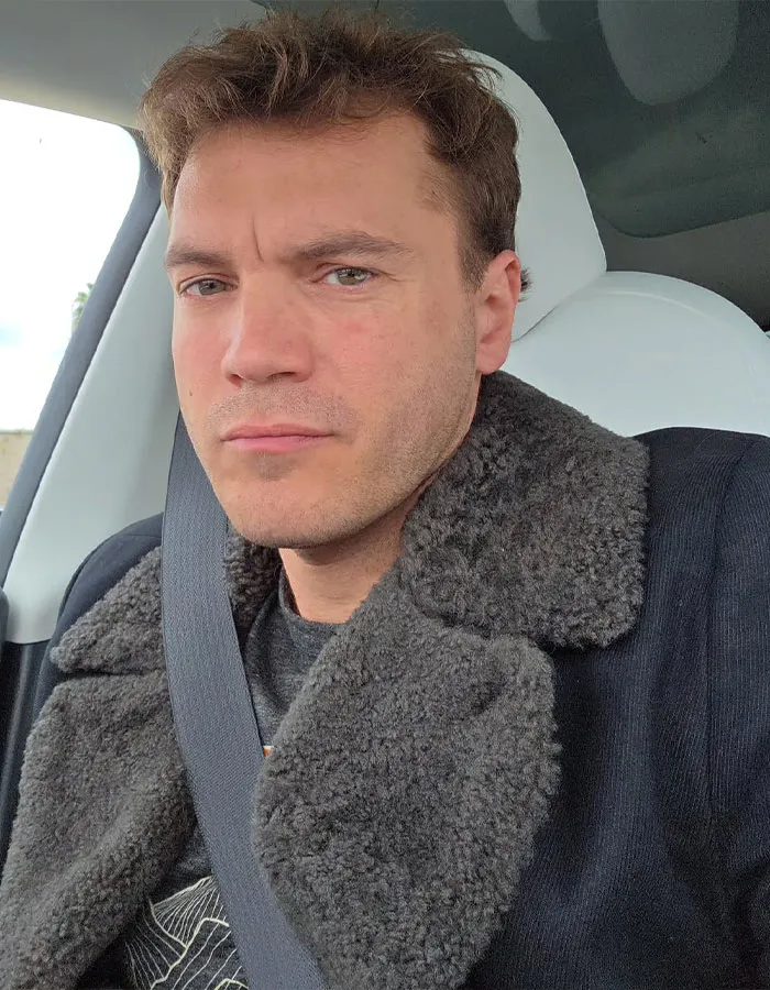 Male star wearing a black coat with a shearling collar, seated in a car, representing male stars height shock factor.