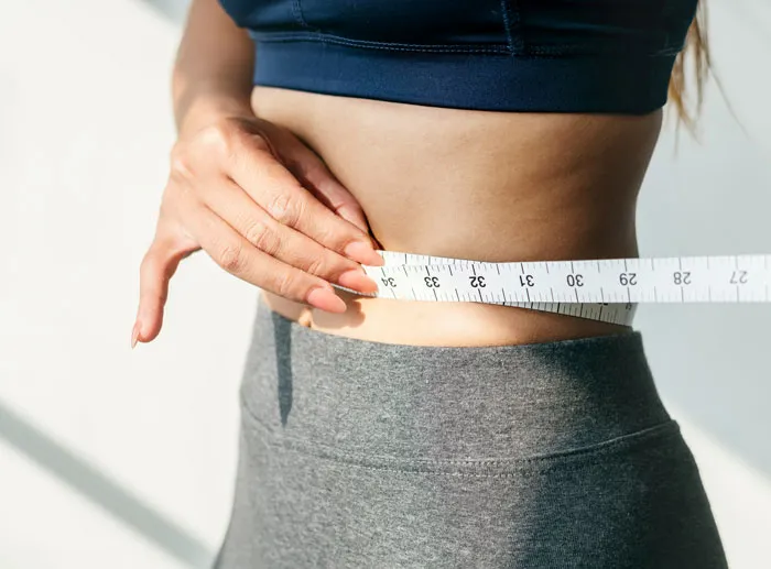 Close-up of a person measuring their waist, illustrating plastic surgeons and unnecessary surgeries related to body contouring.