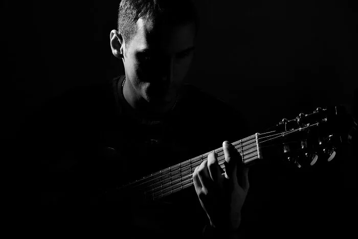 Man playing guitar in low light, evoking mind-bending scenarios that challenge morals and personal reflection.