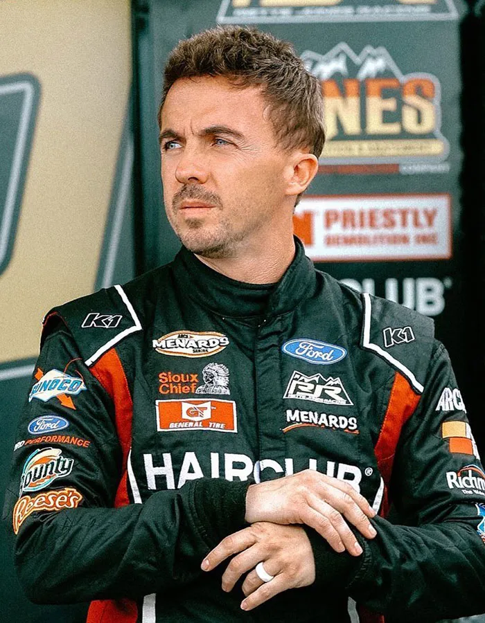 Male star wearing a racing suit with sponsor logos, captured in a candid moment highlighting surprising actual height.