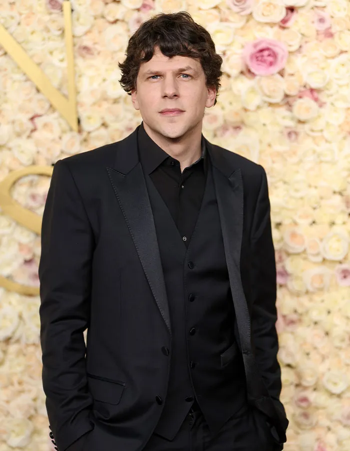 Hombre famoso con traje negro posando frente a fondo con flores, relacionado con celebridades masculinas y estatura sorprendente.