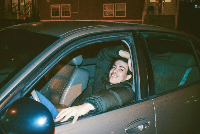 Teen boy smiling confidently while sitting in a car at night, illustrating shocking things popular kids did in school.