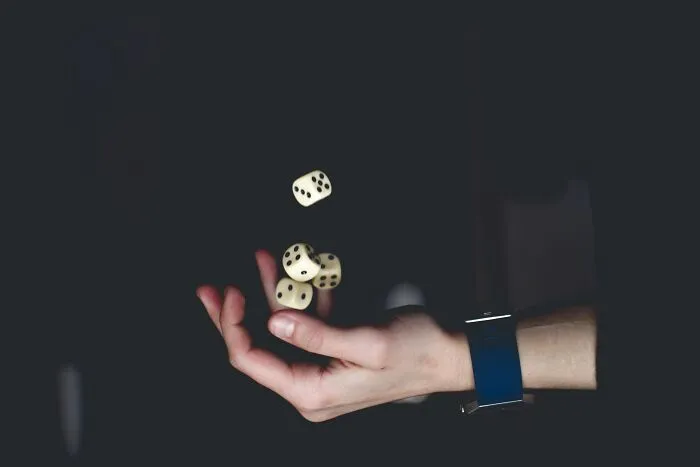 Hand tossing four dice in the air against a dark background, illustrating mind-bending scenarios that challenge your morals.