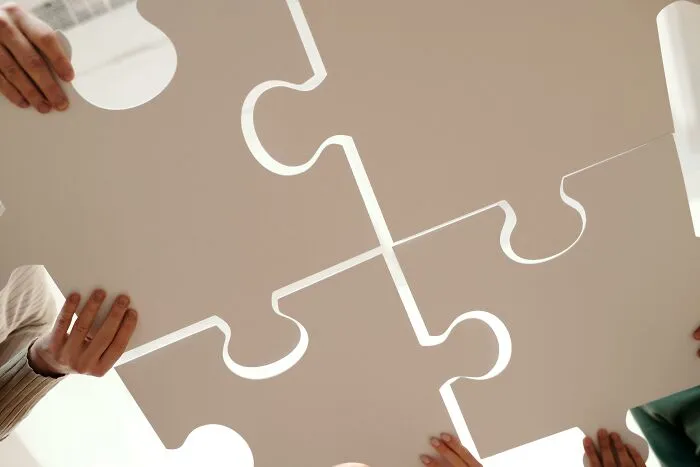 Four hands holding large puzzle pieces fitting together, symbolizing mind-bending scenarios that challenge your morals.