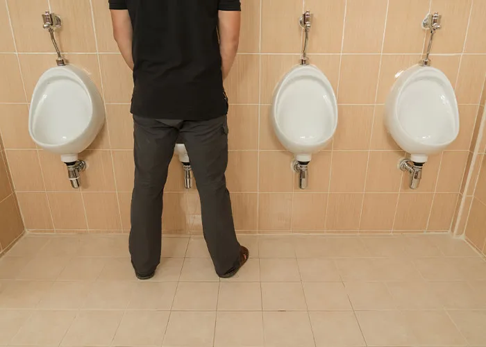 Man standing at urinals in a public restroom, illustrating common myths about men in everyday situations.