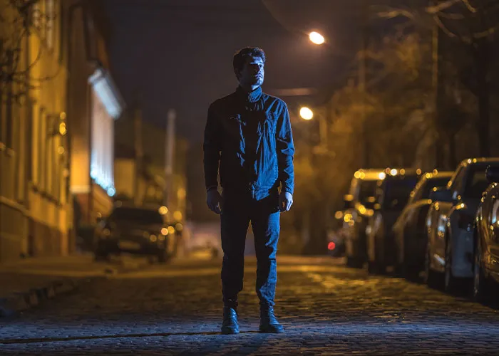Man standing alone on a dimly lit street at night, representing common myths about men that are untrue.