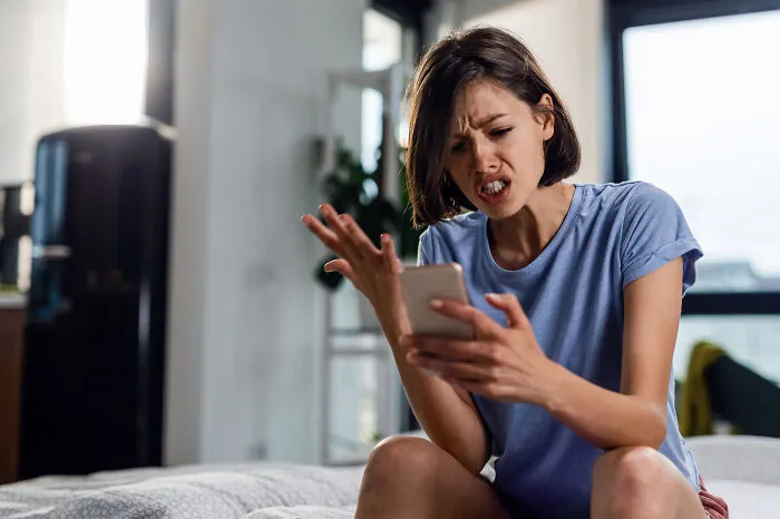 Woman looking frustrated and upset while making a strange 911 call on her phone in a modern home setting.