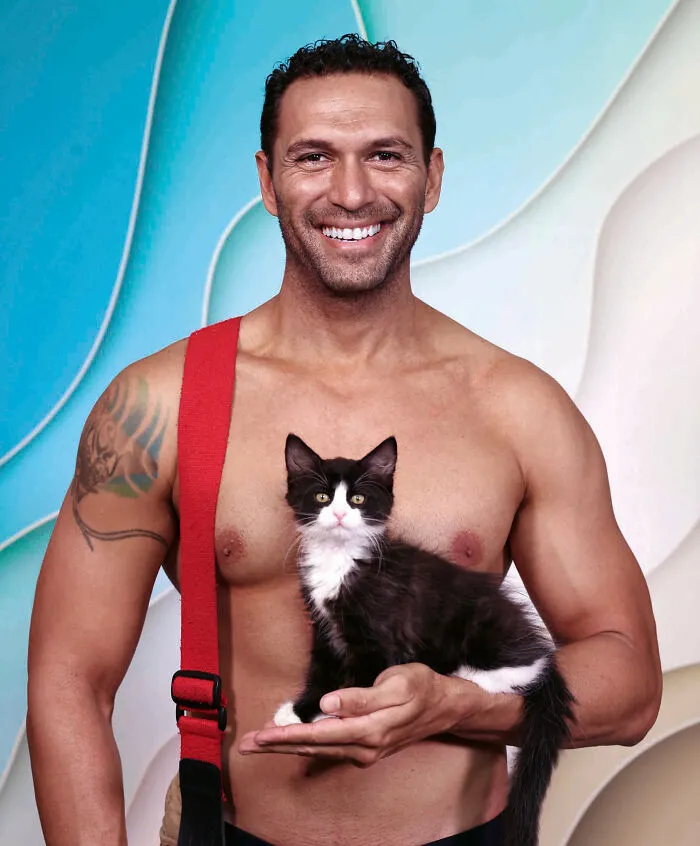 Shirtless Australian firefighter holding a black and white kitten, featured in a firefighters calendar with kittens.