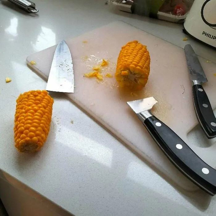 Trozos de mazorca de maíz y cuchillos con formas extrañas en una tabla de cocina, imagen bizarra y rara.