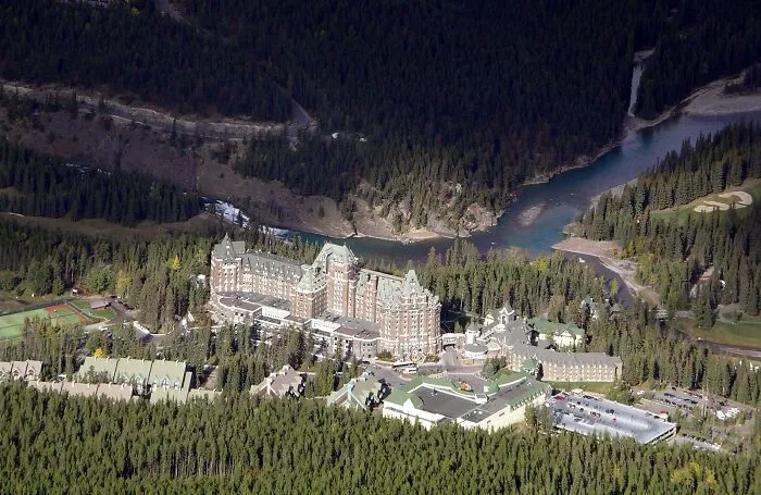 Aerial view of a large historic castle surrounded by dense forest and a winding river, a spooky destination for Halloween.