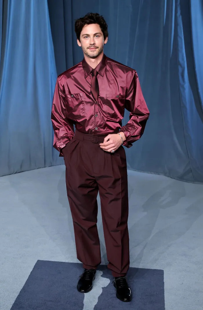 Hombre con camisa satinada y pantalones burdeos posando en gala del museo de la academia moda 2025.