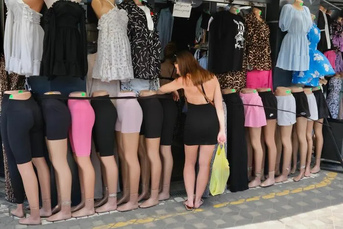 Woman in a black dress browsing street market mannequins wearing various skirts and dresses in pure street photography awards style.